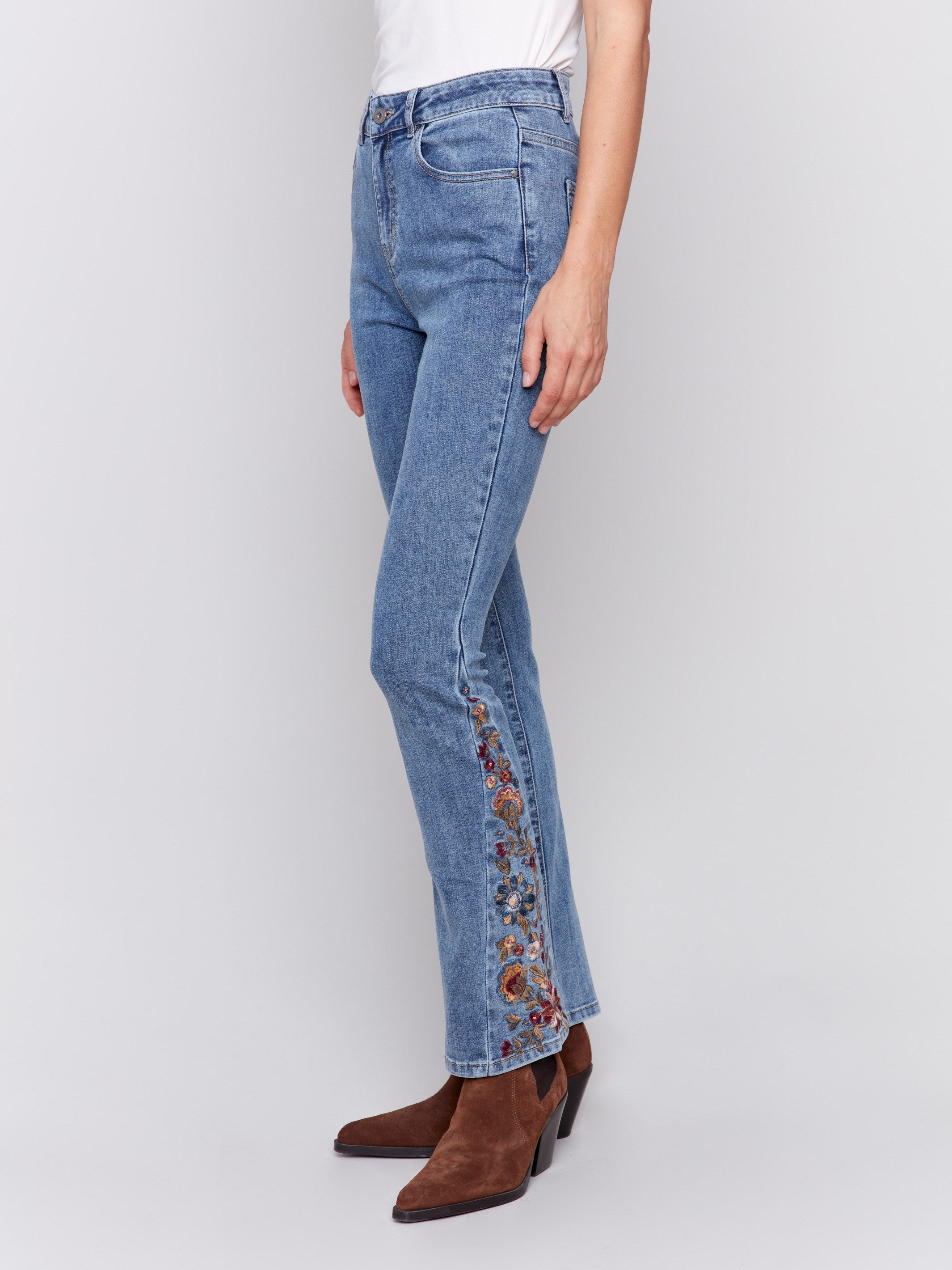 Medium blue bootcut jeans with vibrant floral embroidery on the sides and a classic five-pocket design by Charlie B.