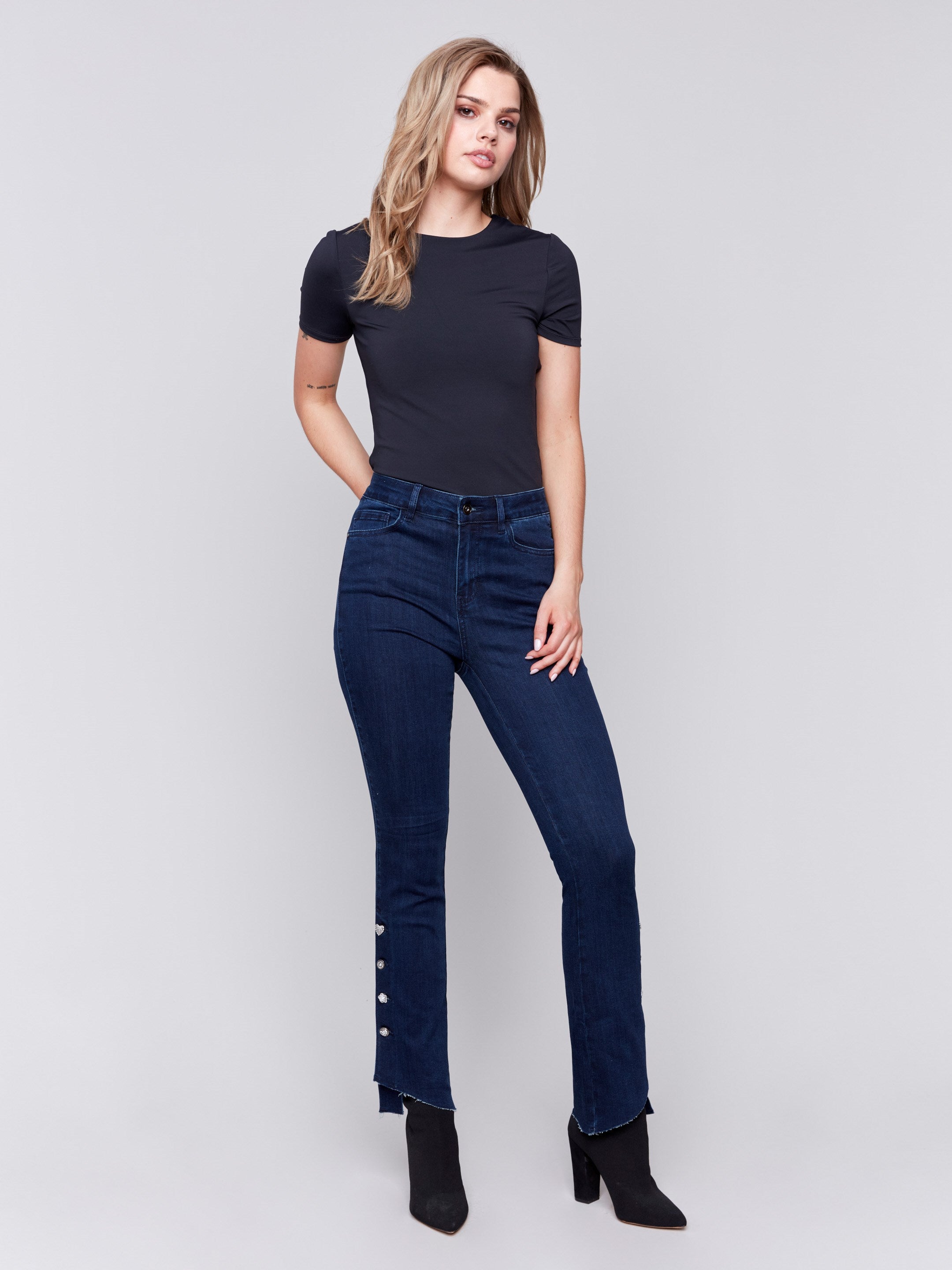 Dark blue-black bootcut jeans with gem buttons and a raw edge hem, featuring a five-pocket design by Charlie B.