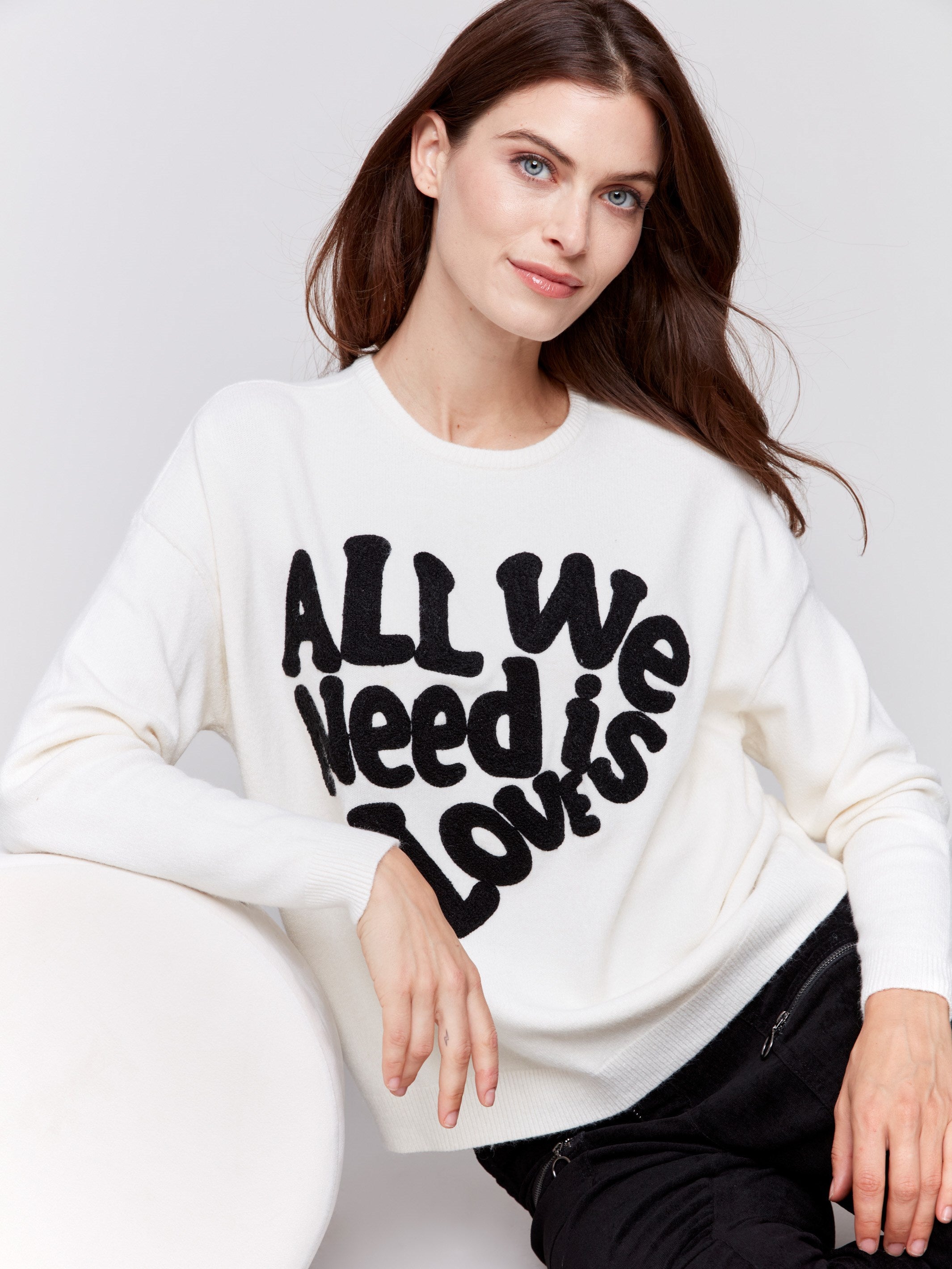 Ecru white crew neck sweater with black 'All We Need is Love' embroidery, featuring a drop shoulder design and long sleeves by Charlie B.