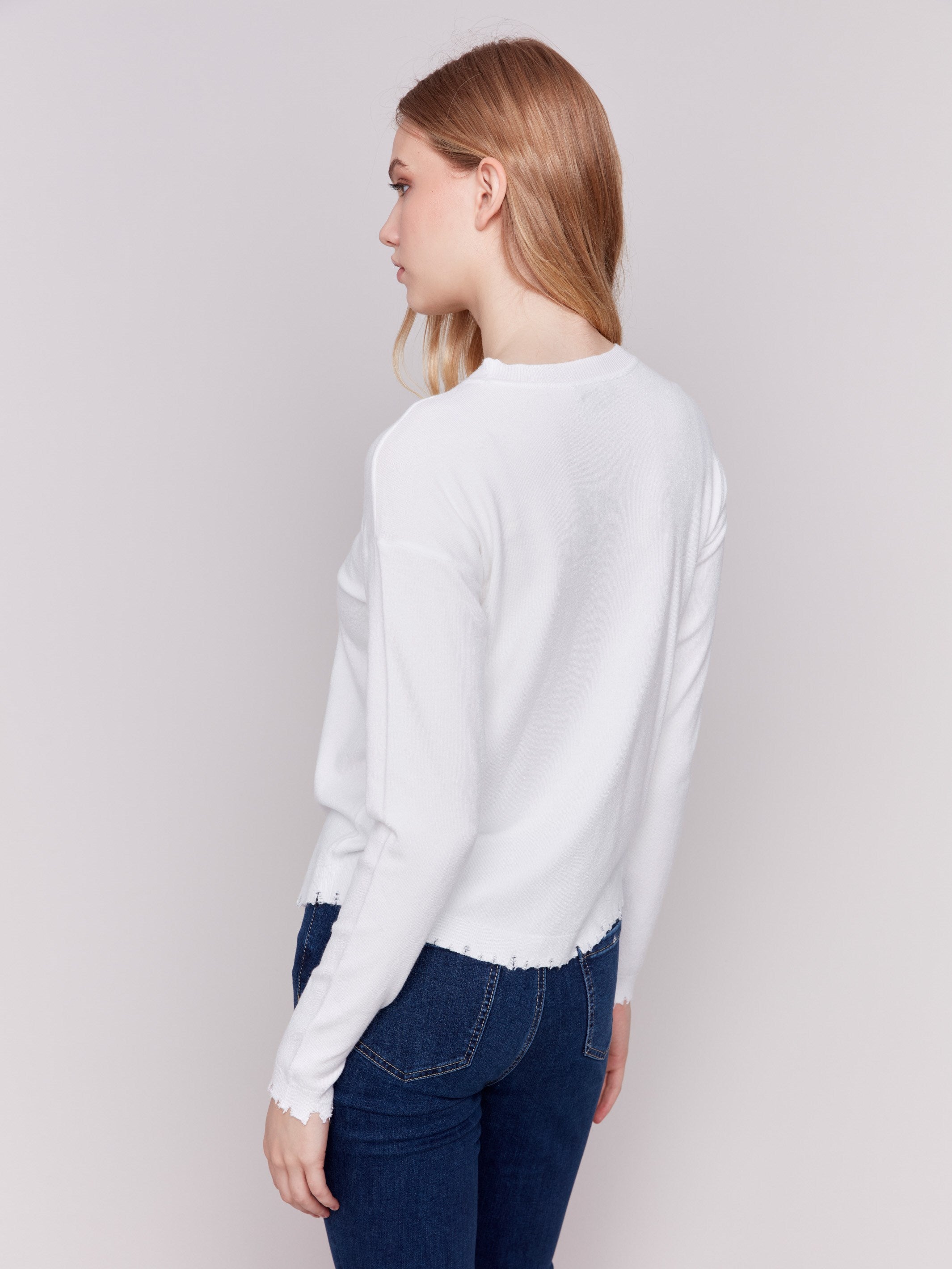 Cream white long-sleeve sweater with a crew neck and frayed rounded hem by Charlie B.