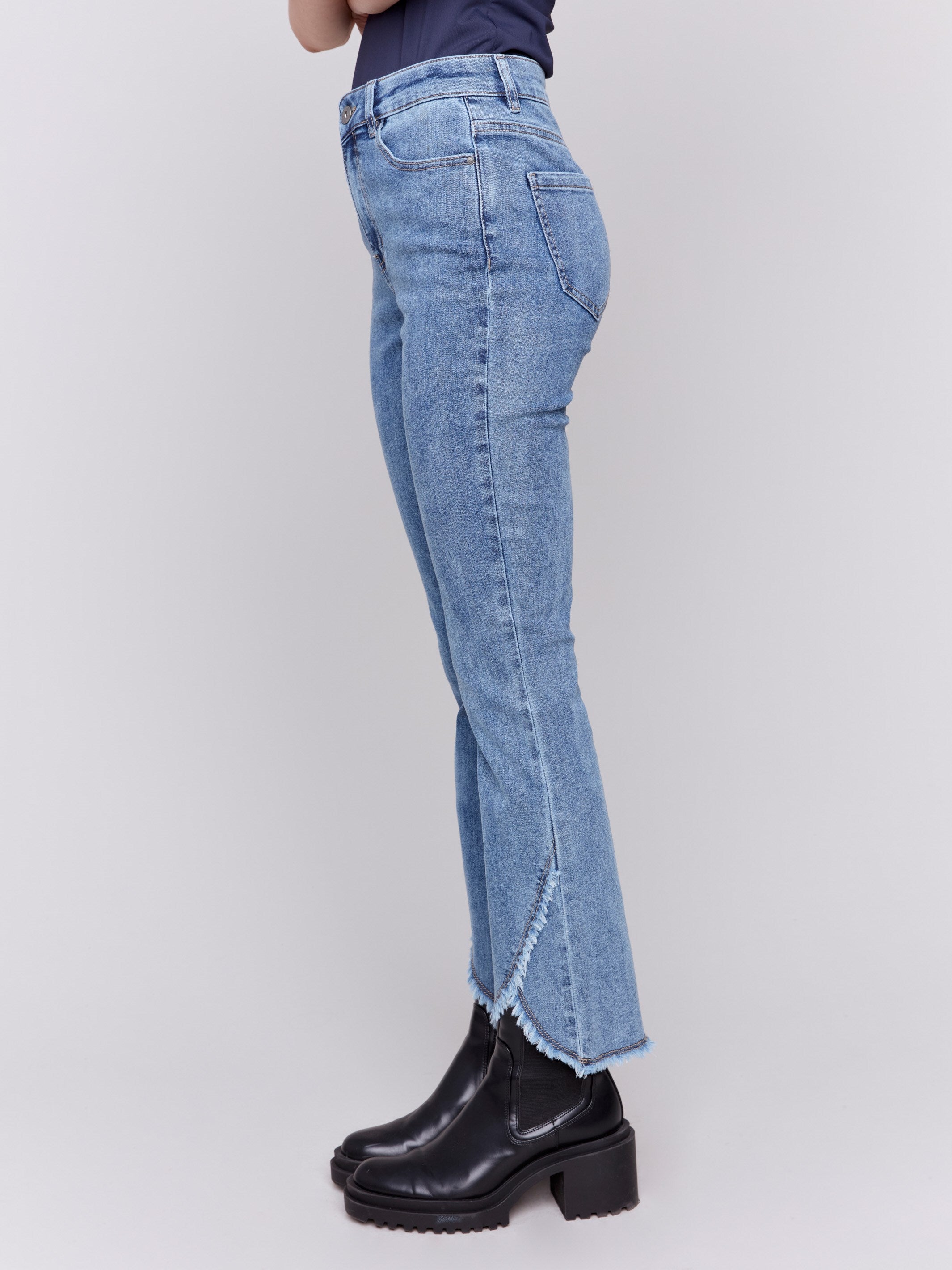 Medium blue denim jeans with a tulip hem and bootcut design by Charlie B. Featuring a mid-rise and frayed hem details.