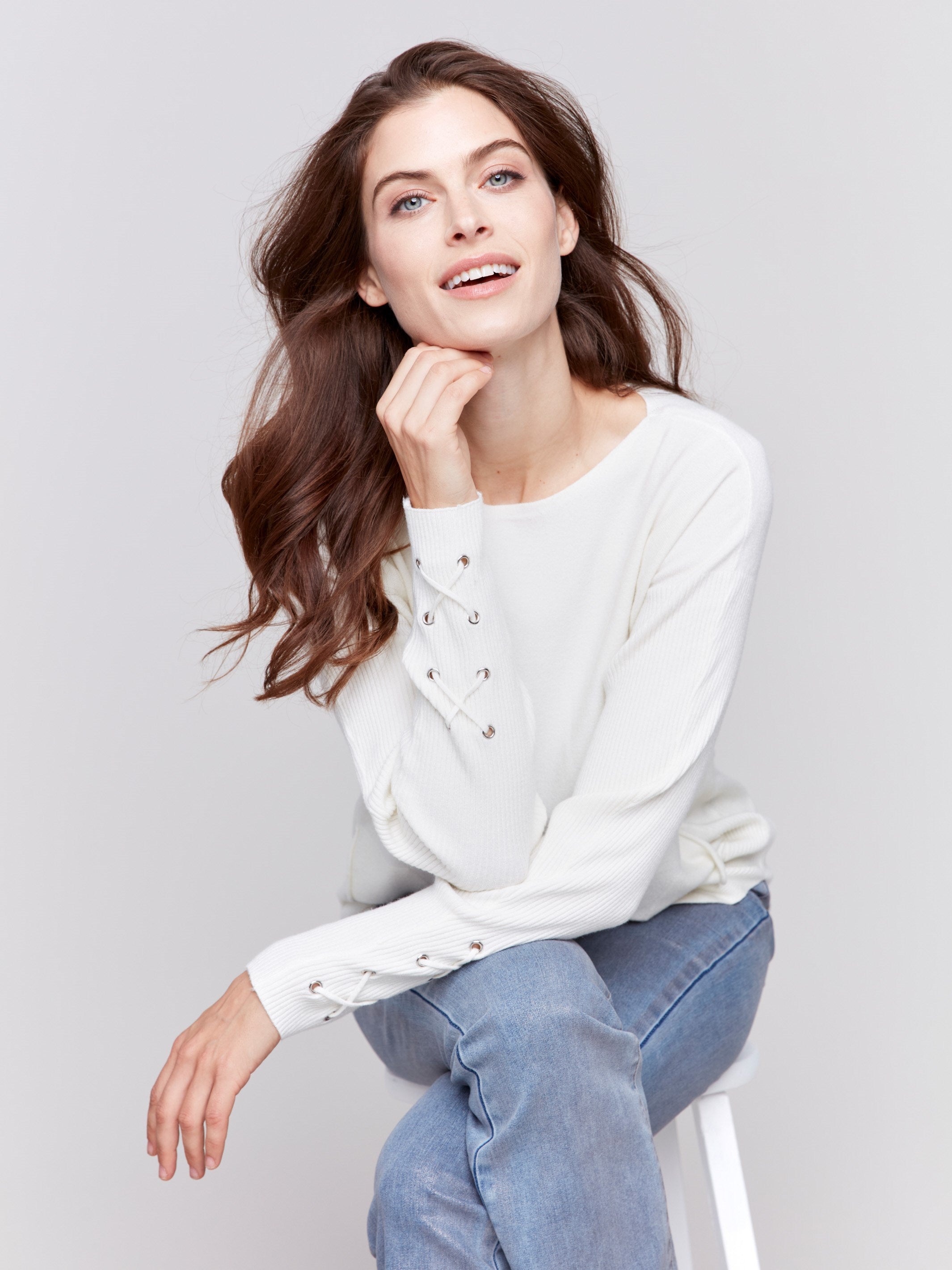 Ecru white long-sleeved knit sweater with lace-up cuffs, rounded hem, and front pockets by Charlie B.