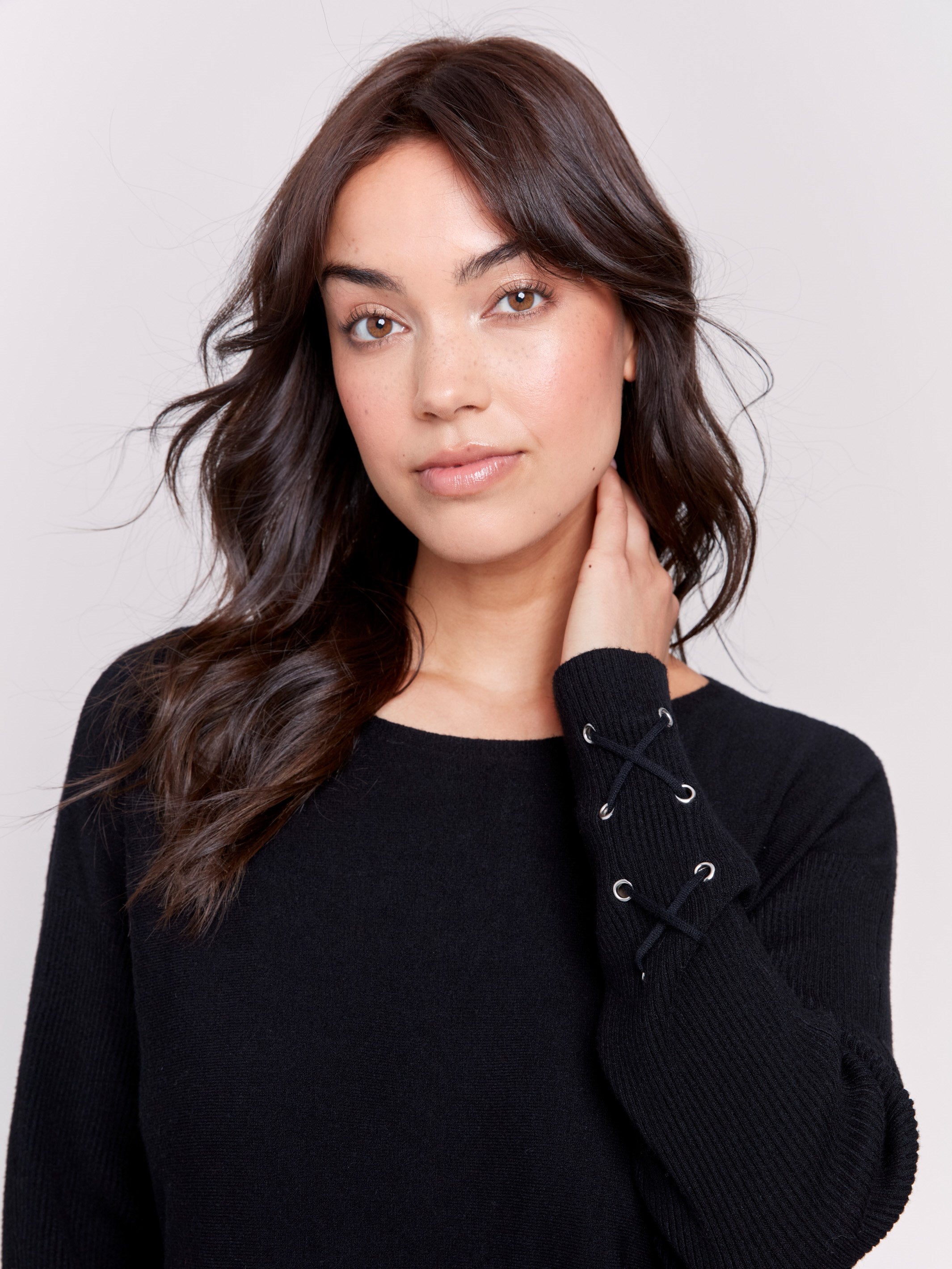 Black long-sleeved knit sweater with lace-up cuffs, rounded hem, and front pockets by Charlie B.