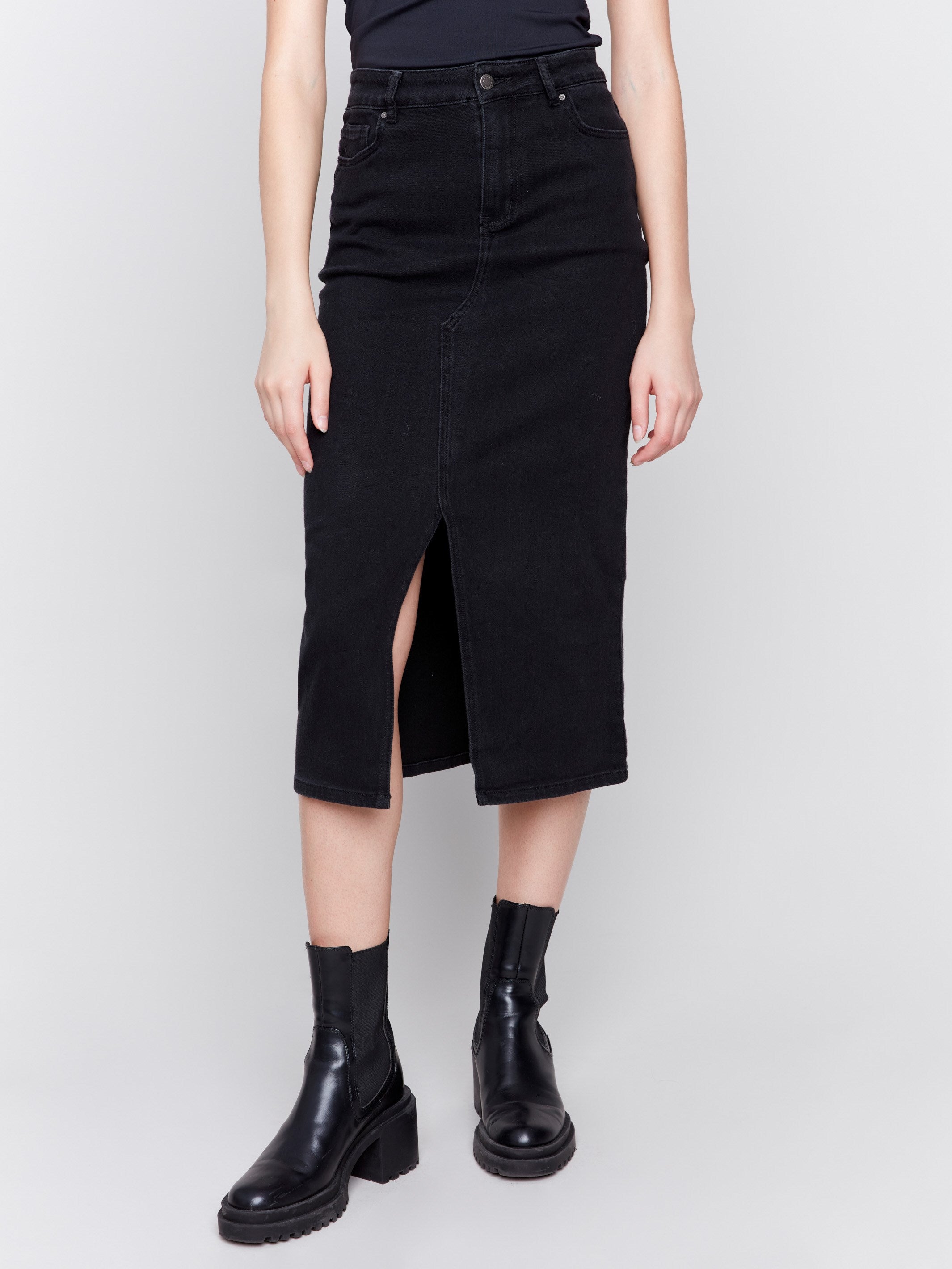 Charcoal black midi-length denim skirt with front slit, featuring a mid-rise waist and slim fit, paired with boots by Charlie B.