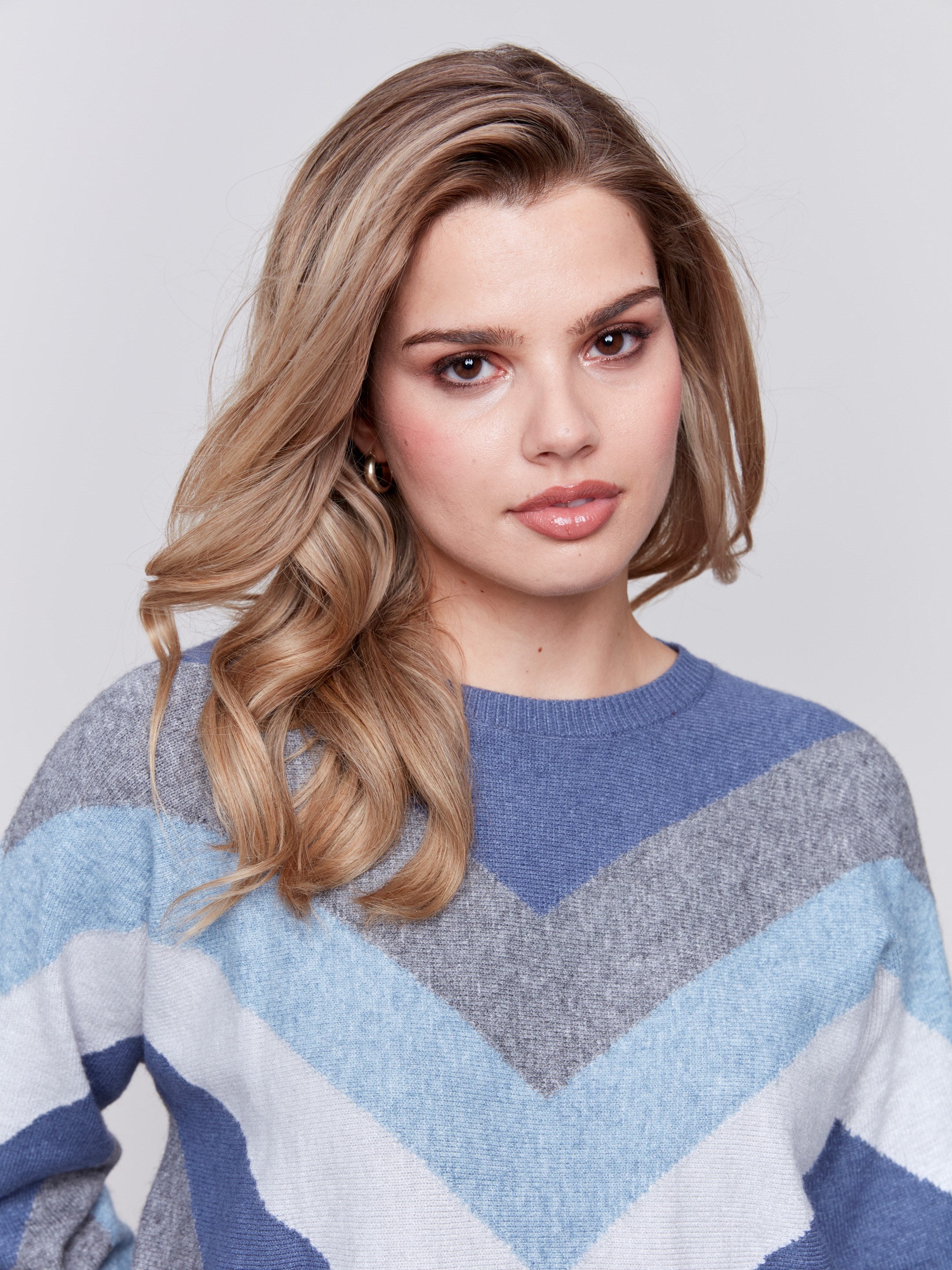 Denim-colored long-sleeve sweater with chevron stripes in blue, grey, and white. Crew neckline and ribbed cuffs by Charlie B.