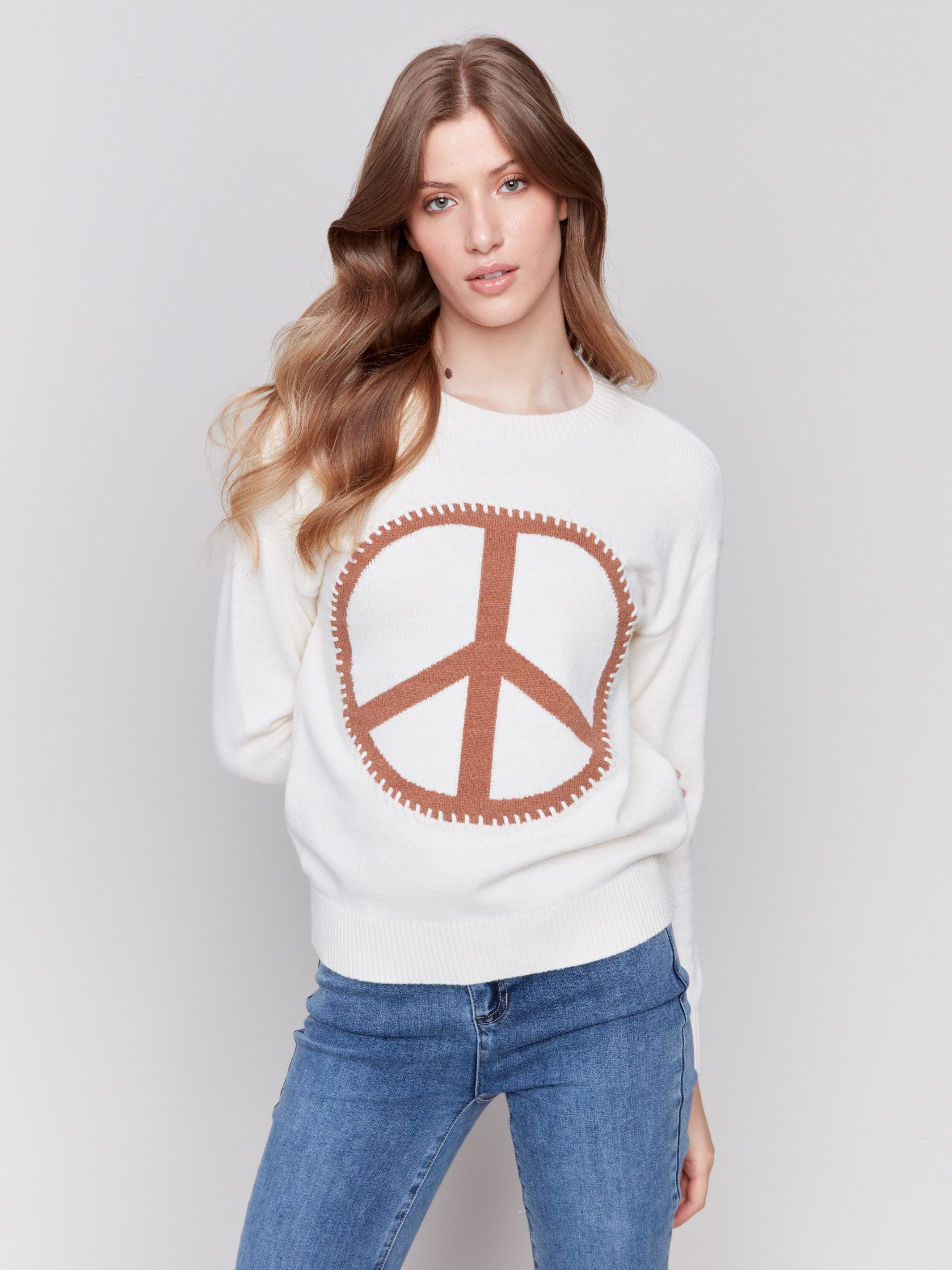 Ecru white sweater featuring a large peace sign graphic on the front with blanket stitch detailing, long sleeves, and crew neckline by Charlie B.