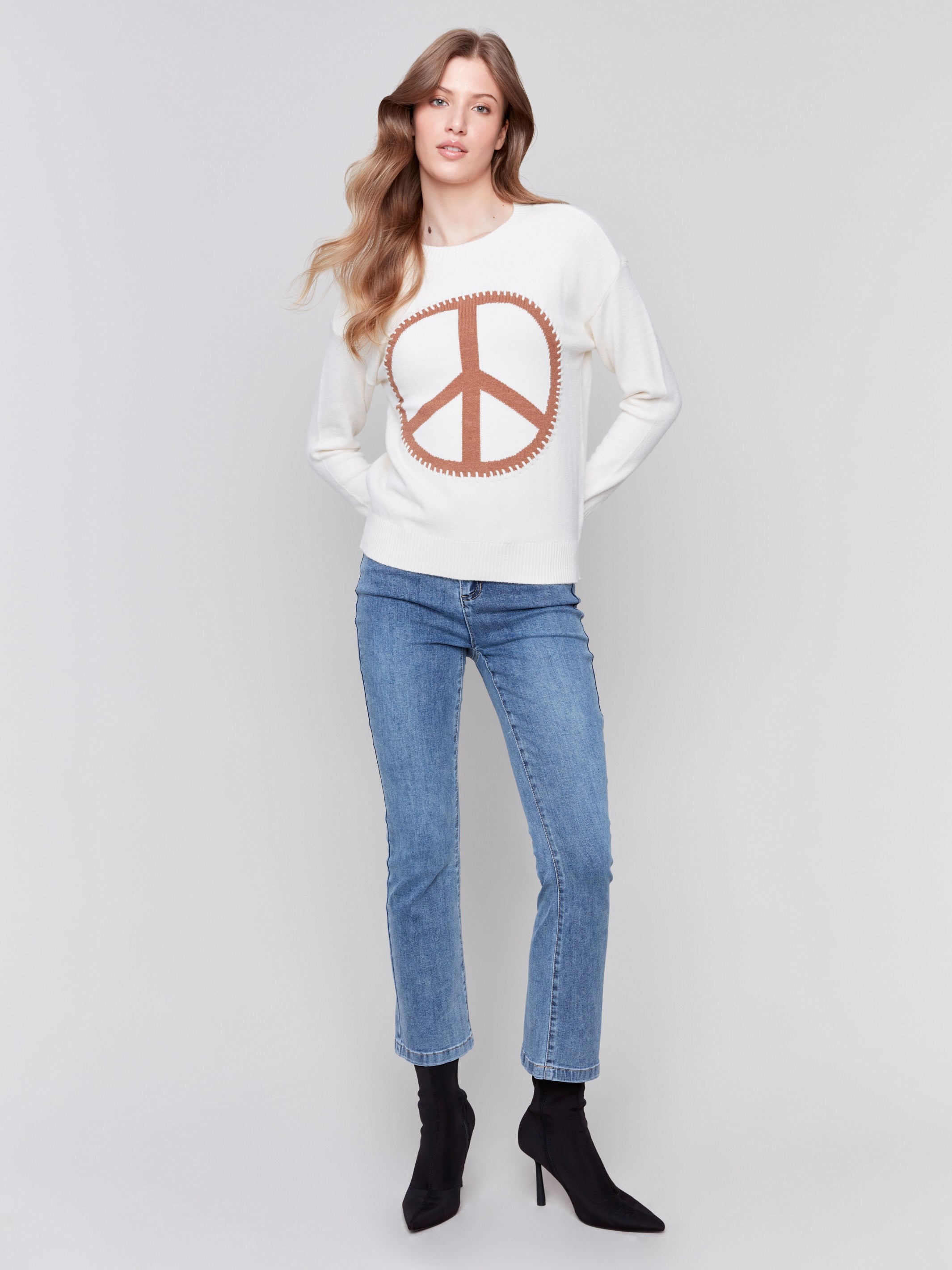 Ecru white sweater featuring a large peace sign graphic on the front with blanket stitch detailing, long sleeves, and crew neckline by Charlie B.