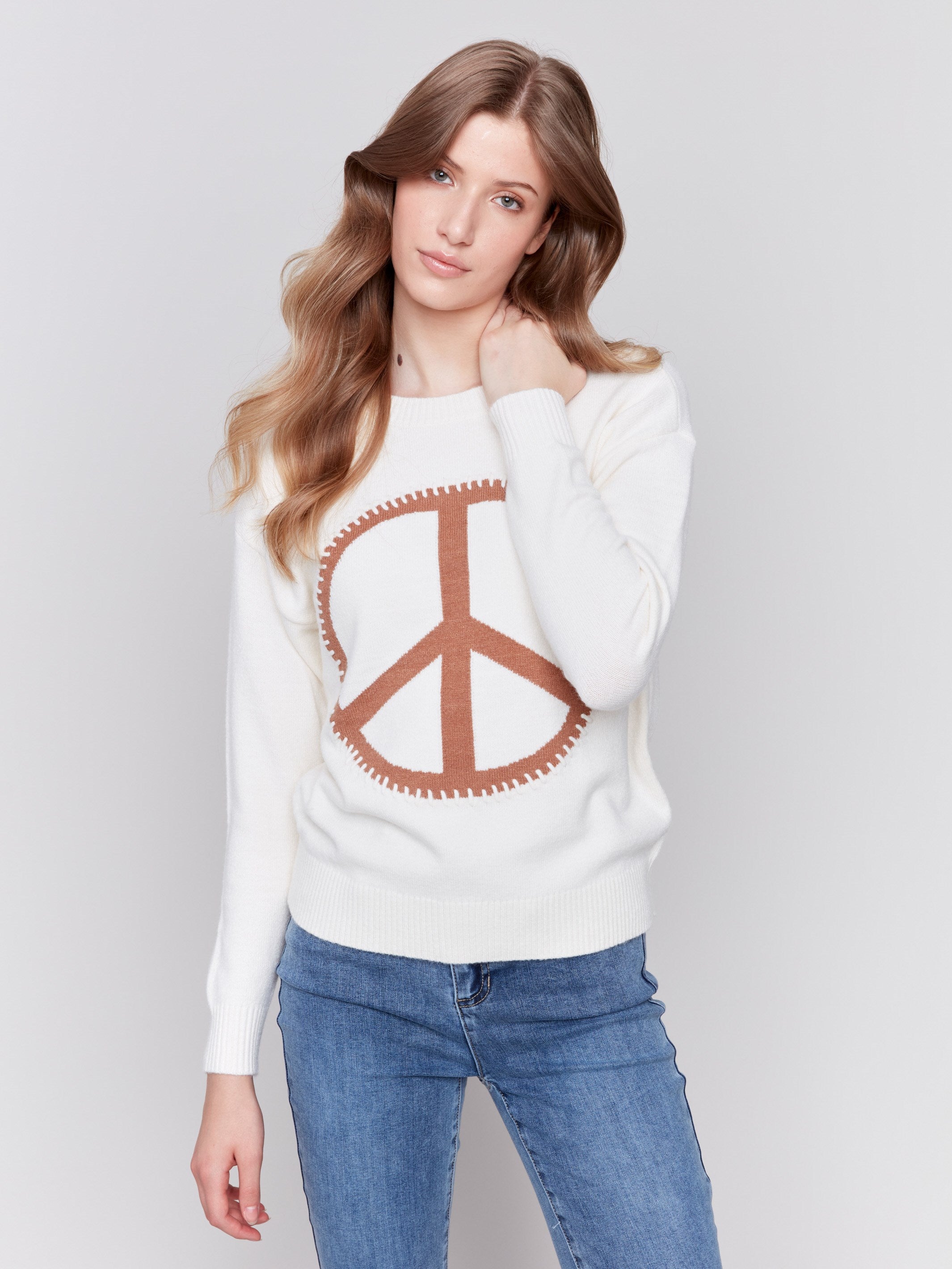 Ecru white sweater featuring a large peace sign graphic on the front with blanket stitch detailing, long sleeves, and crew neckline by Charlie B.