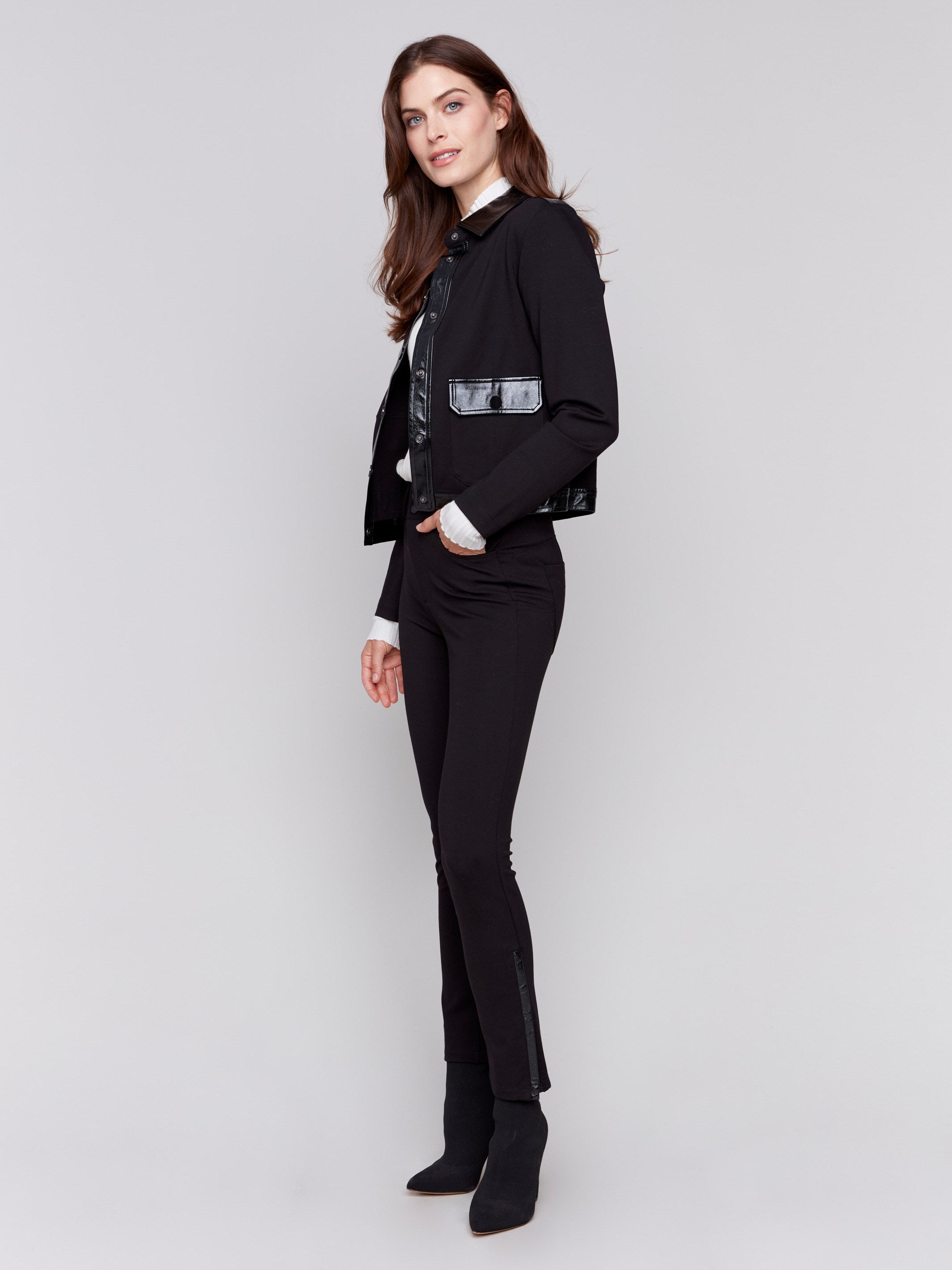 Short black jacket with glossy vinyl trim, featuring front flap pockets and a button closure, by Charlie B.