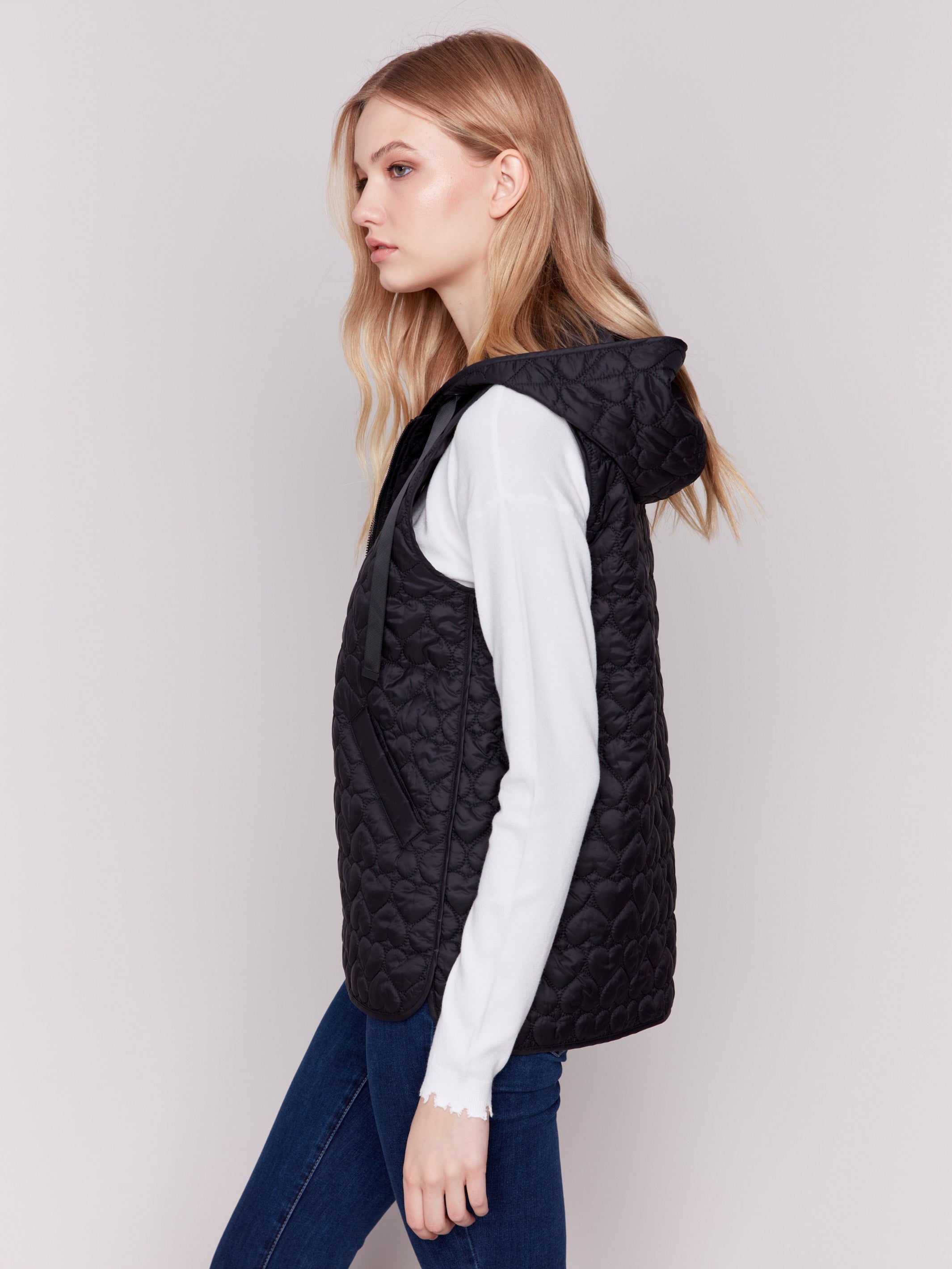 Black short quilted puffer vest with a hood, featuring a mini heart pattern and front pockets by Charlie B.