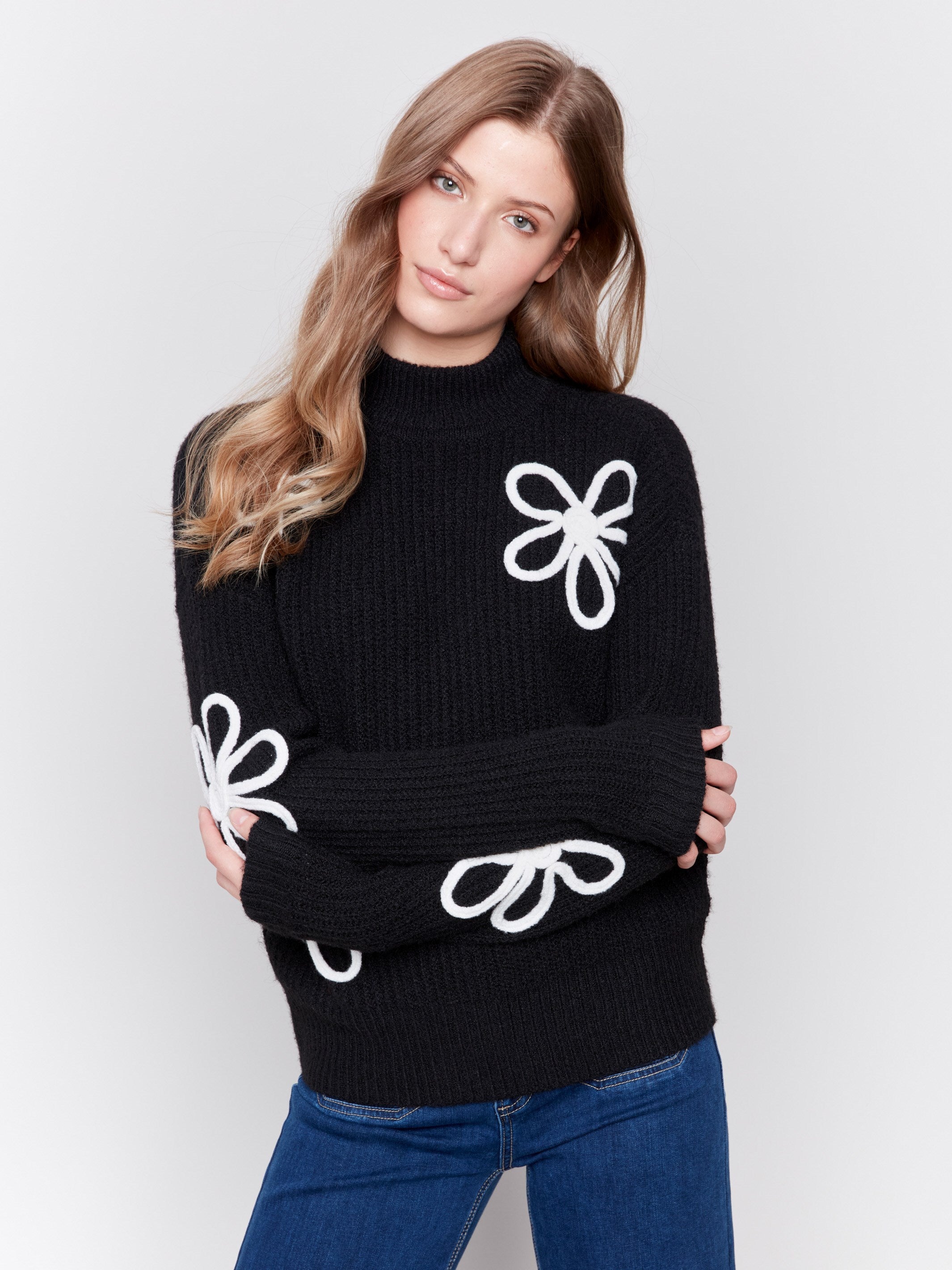 Black mock-neck sweater with white floral embroidery and ribbed texture by Charlie B.